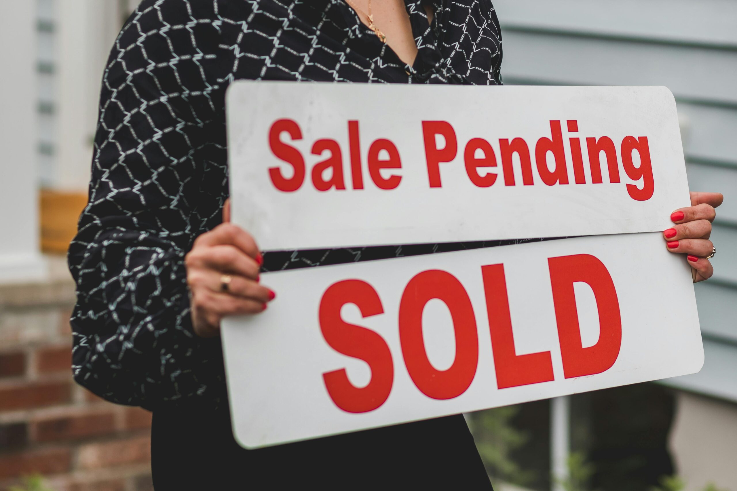 A businesswoman holding 'Sale Pending' and 'Sold' signs indicating a successful real estate transaction.